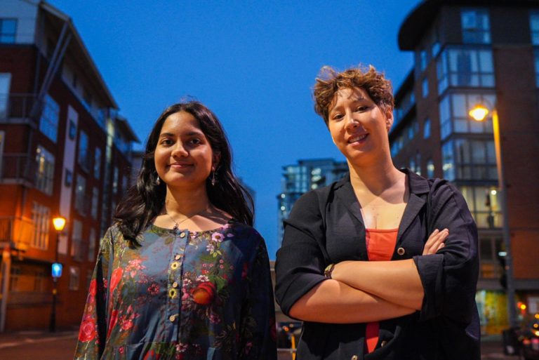 The new Birmingham Poet Laureate and Young Poet Laureate stand in the street at dusk, looking at the camera.